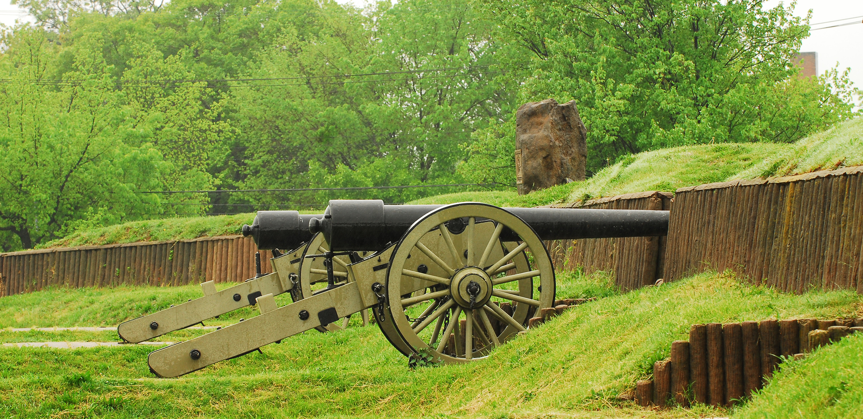 Photograph of two civil-war era cannons placed behind the grass covered ramparts of a brick fort.
