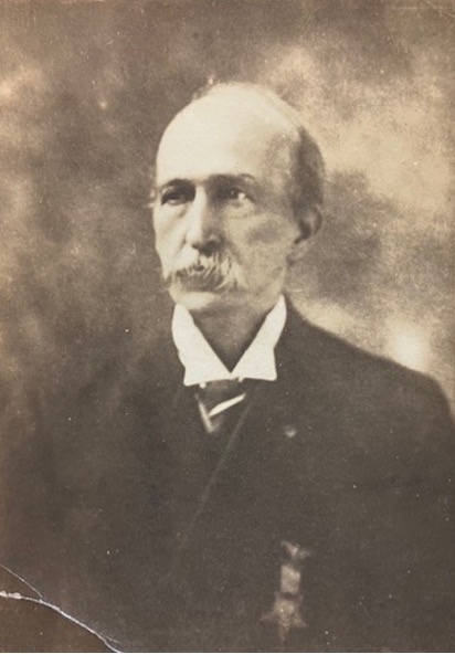 A 19th century photograph of Pension Bureau clerk Lewis Cass White, an elderly man with white hair and a mustache, wearing a black suit and white collared shirt. He gazes to the left reflectively. 