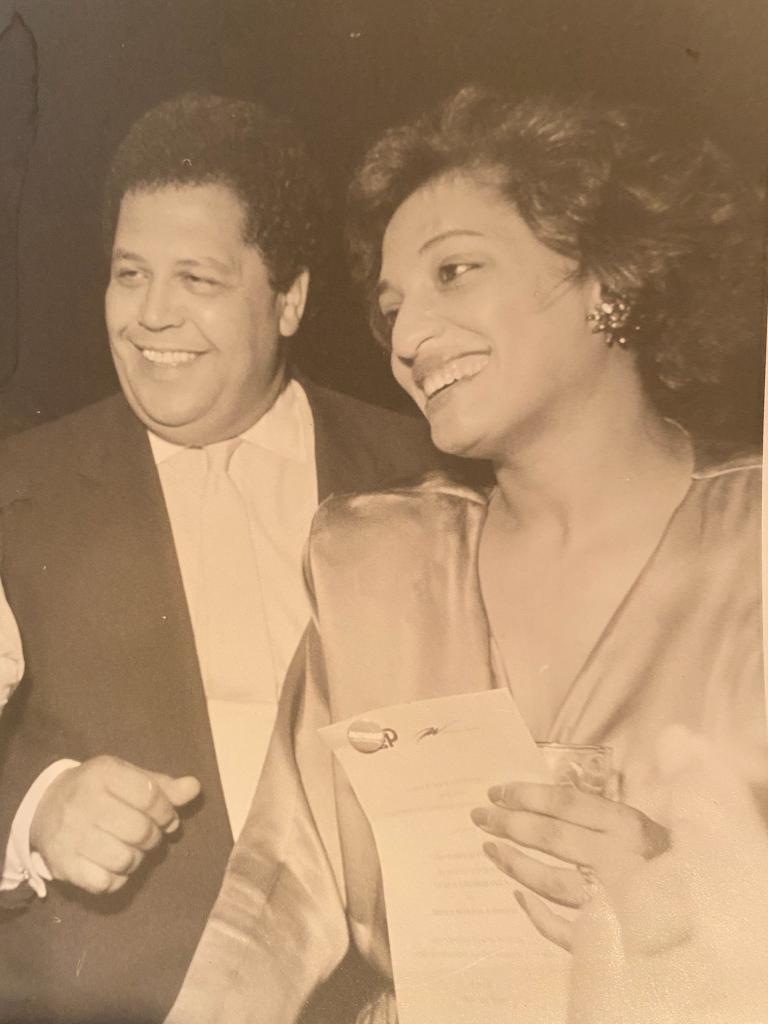 An African American daughter and father together, smiling. Both are dressed in formal wear.