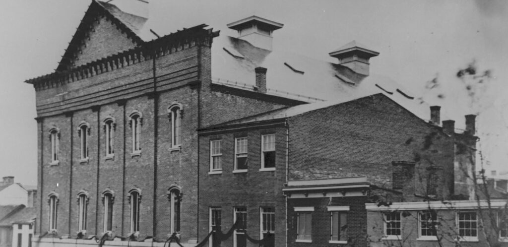 Black and white photograph of Ford's Theatre with black ribbon draped from the windows.