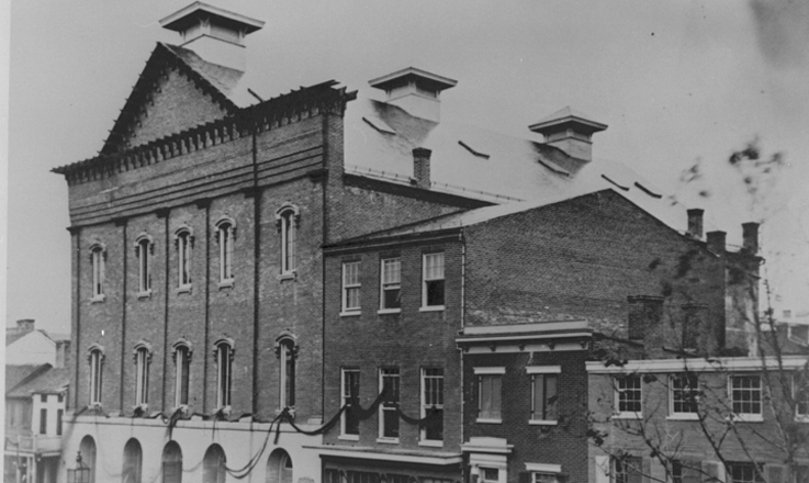 Black and white photograph of Ford's Theatre with black ribbon draped from the windows.