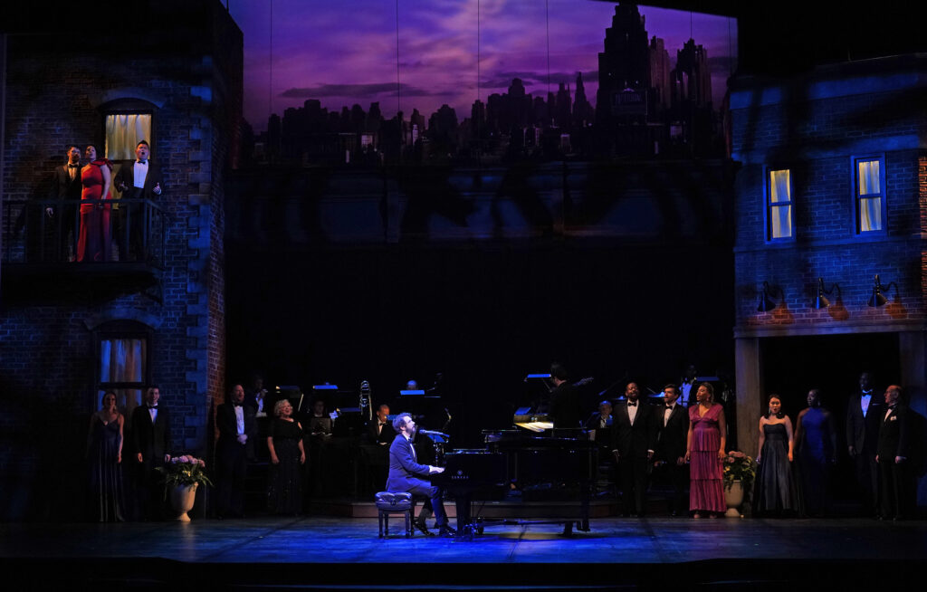 A man plays the piano and sings, while behind him a large group of singers accompany him.