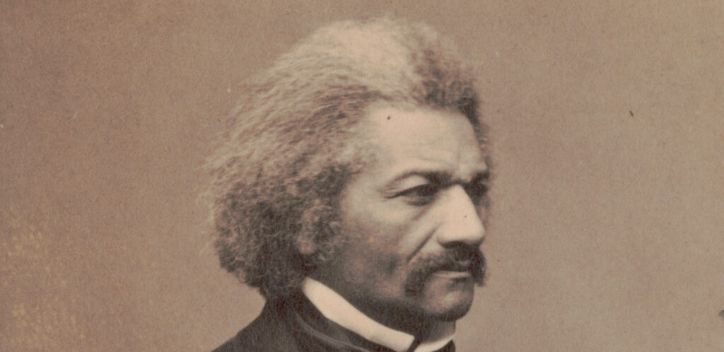 1864 studio photograph of Frederick Douglass seated in ¾ profile, wearing a formal black suit and tie.