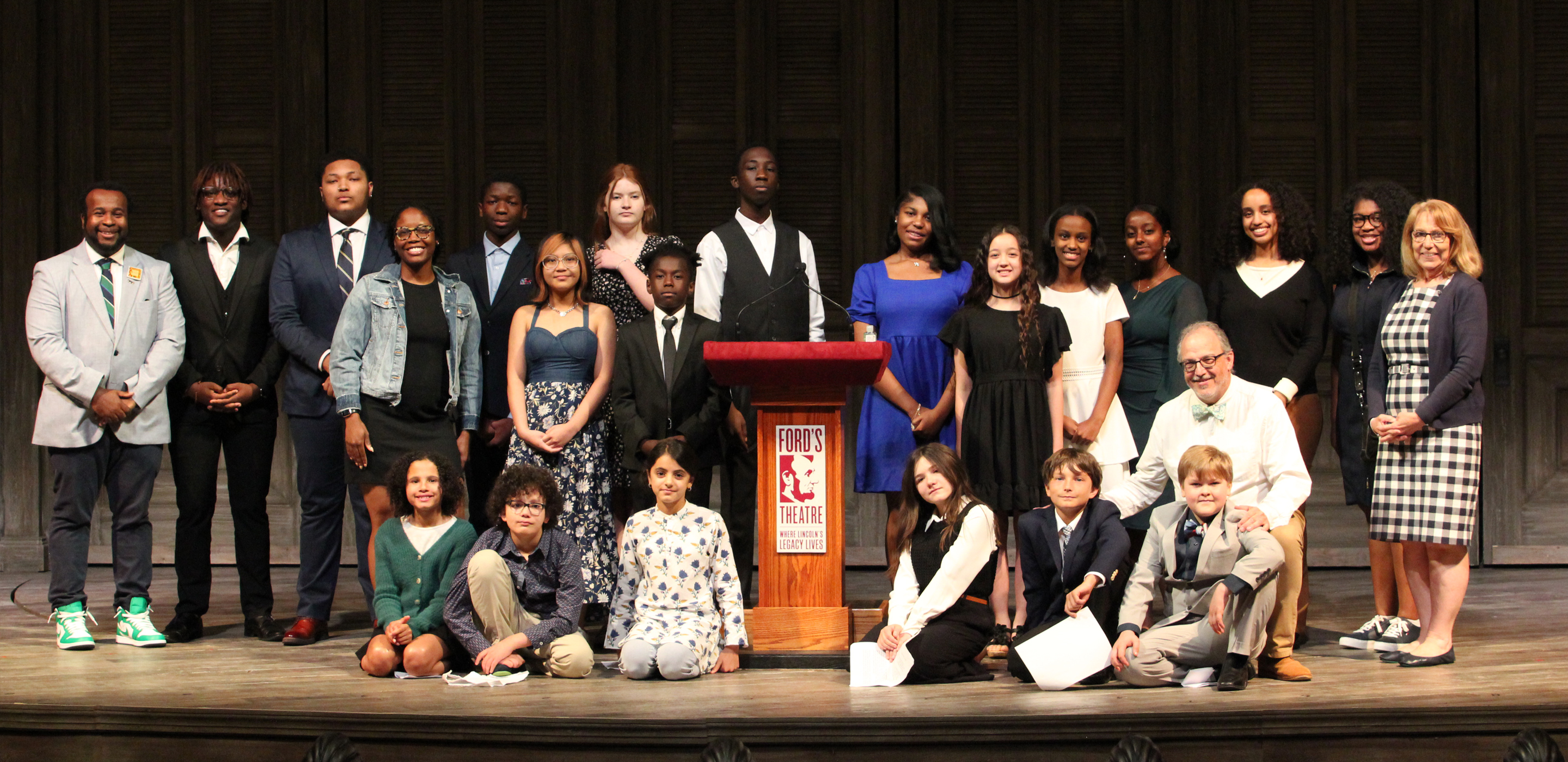 A diverse group of students poses for a picture on a stage.