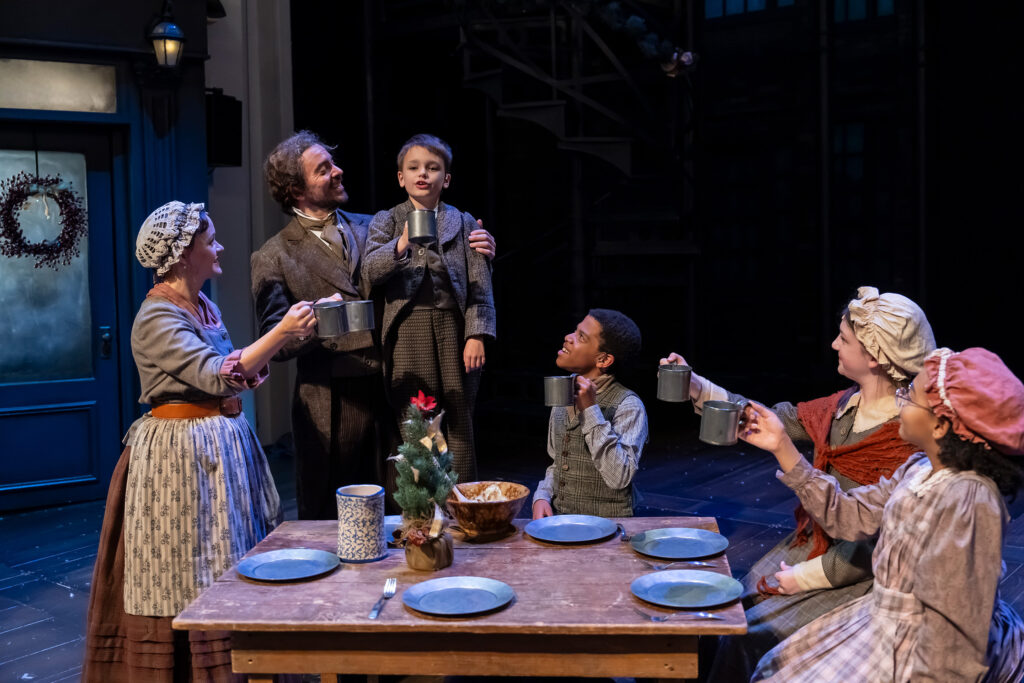 A poor Victorian family shares a holiday toast with tin cups around their dinner table.