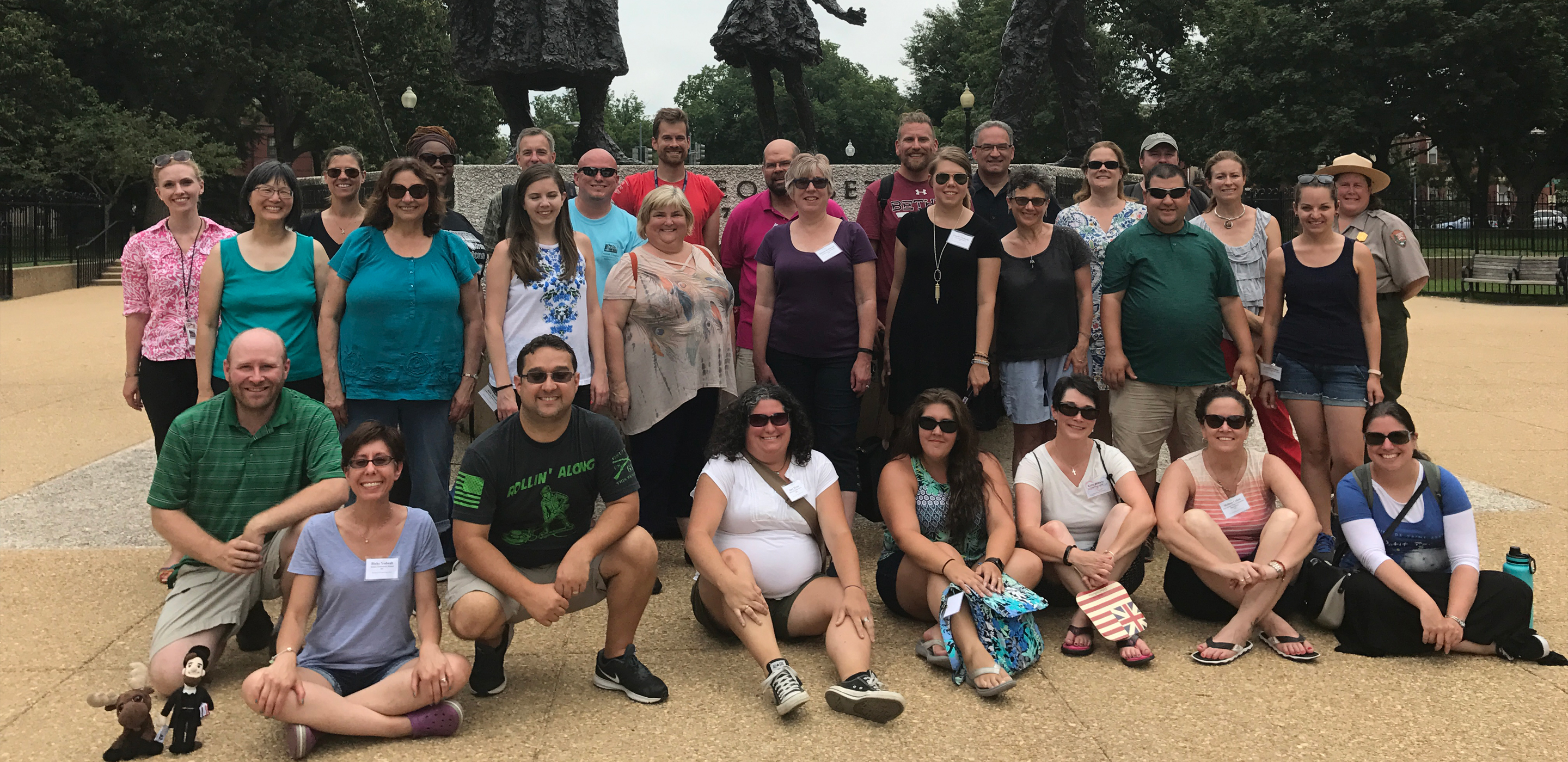 A large group of people stand in front of statues in a park.