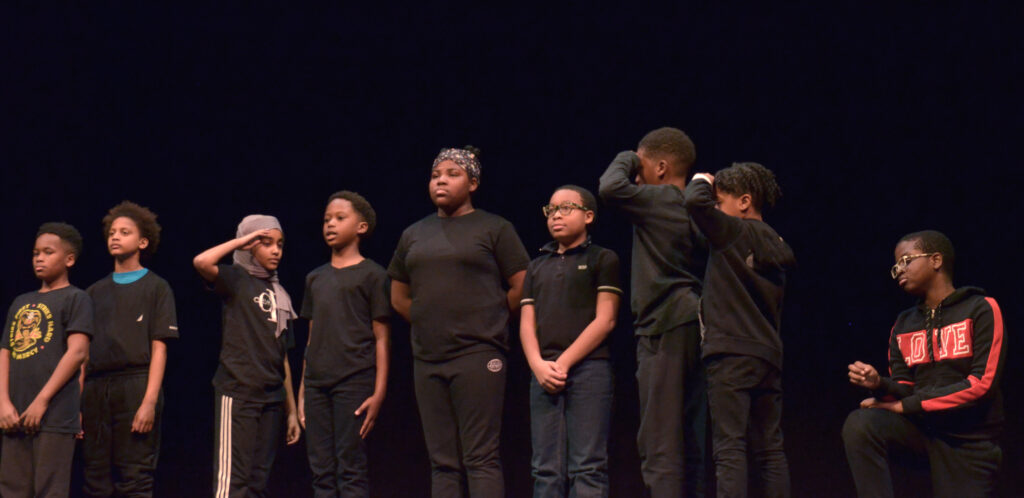 A group of students in black clothing stand on stage and perform a speech.