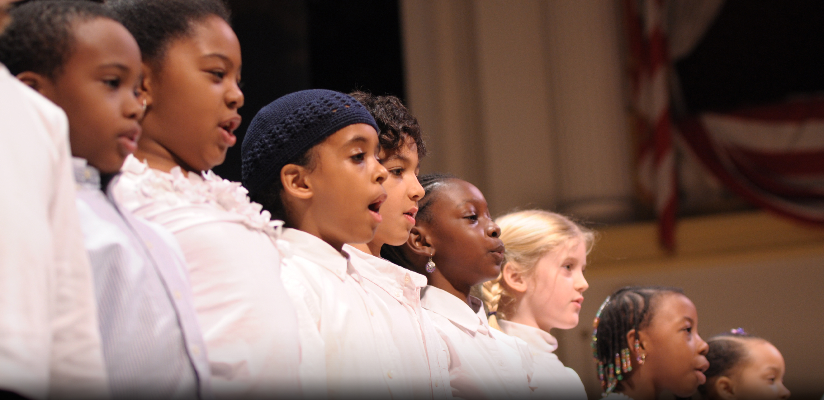 A row of young children in white shirts stand on the Ford's Theatre stage and speak.