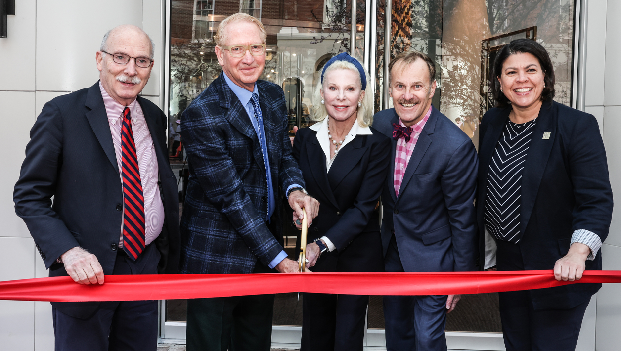 Five people prepare to cut a red ribbon with a large pair of scissors.
