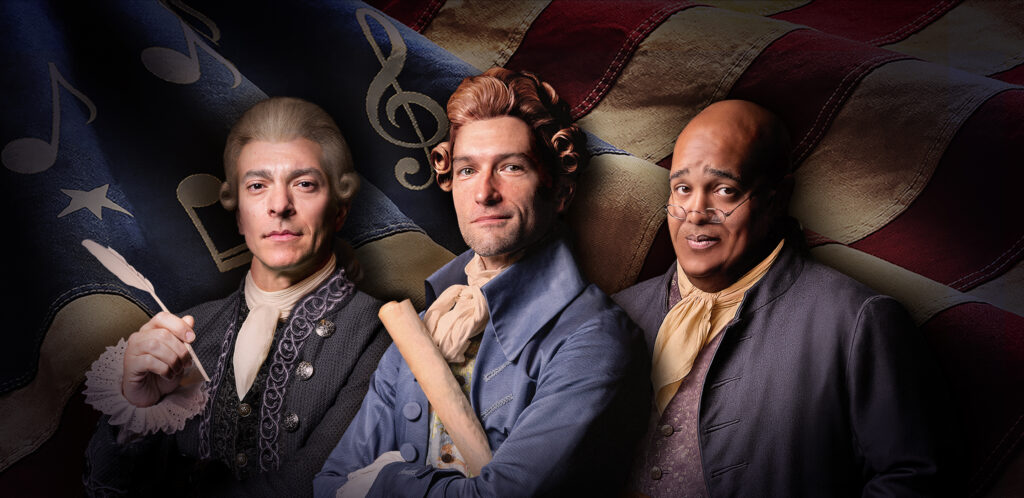Two white men and a Black man dressed in colonial American clothing standing in front of a waving American flag.