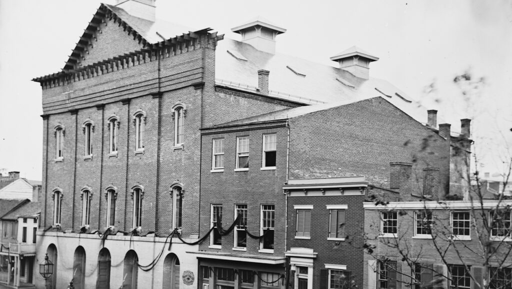Black and white photograph of Ford's Theatre with black ribbon draped from the windows.