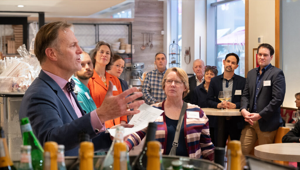 A man stands in front of a crowd gathered in a reception room and gives a speech.