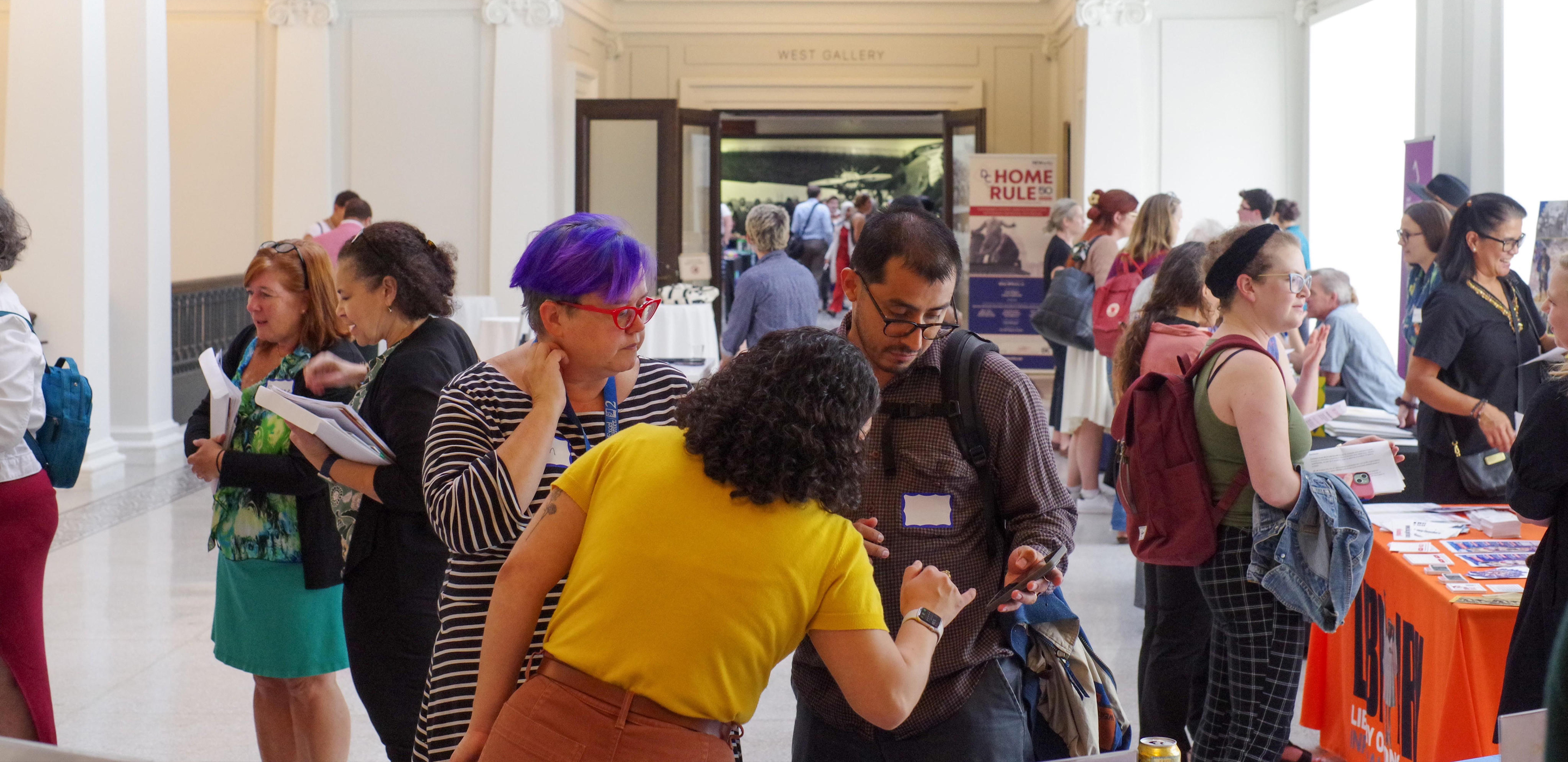 A group of people milling together in a hallway, next to some convention booths.