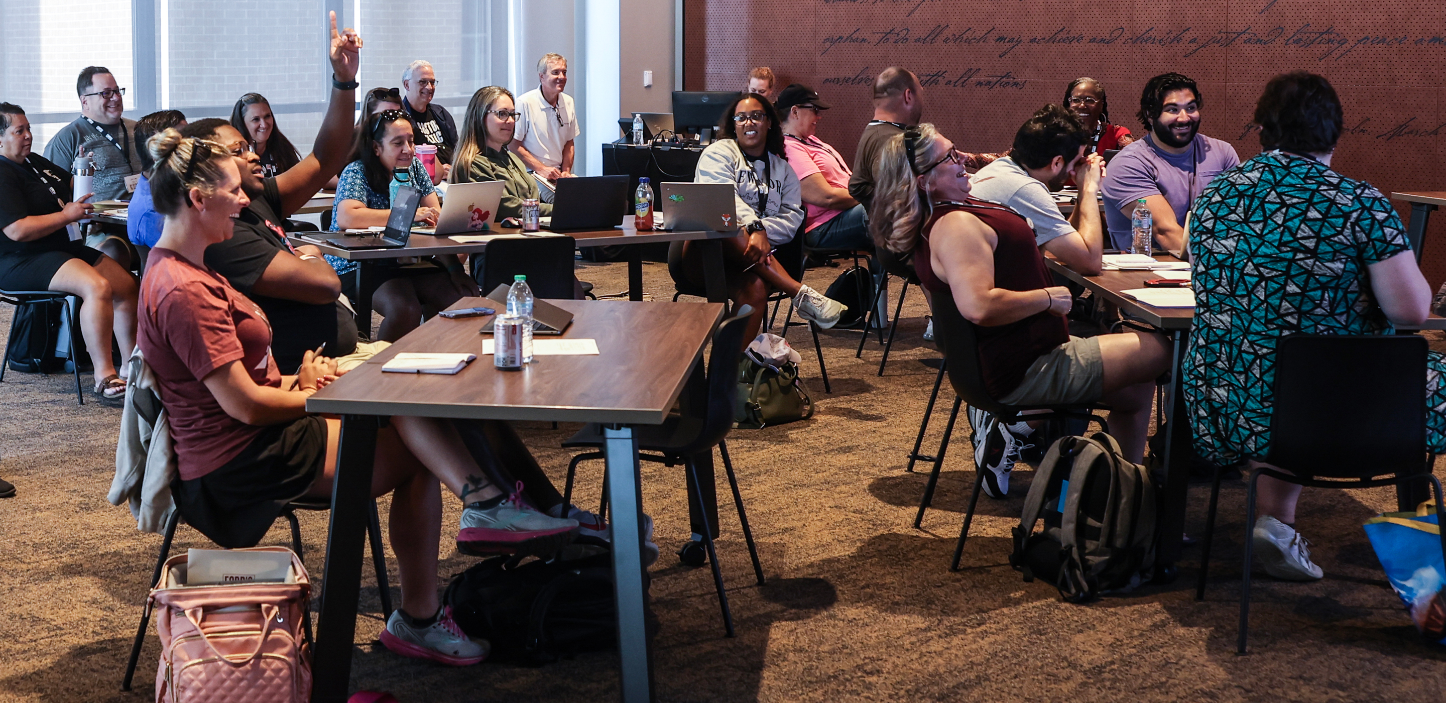 A group of 20 teachers in a meeting room and laughing and engaged in a presentation.