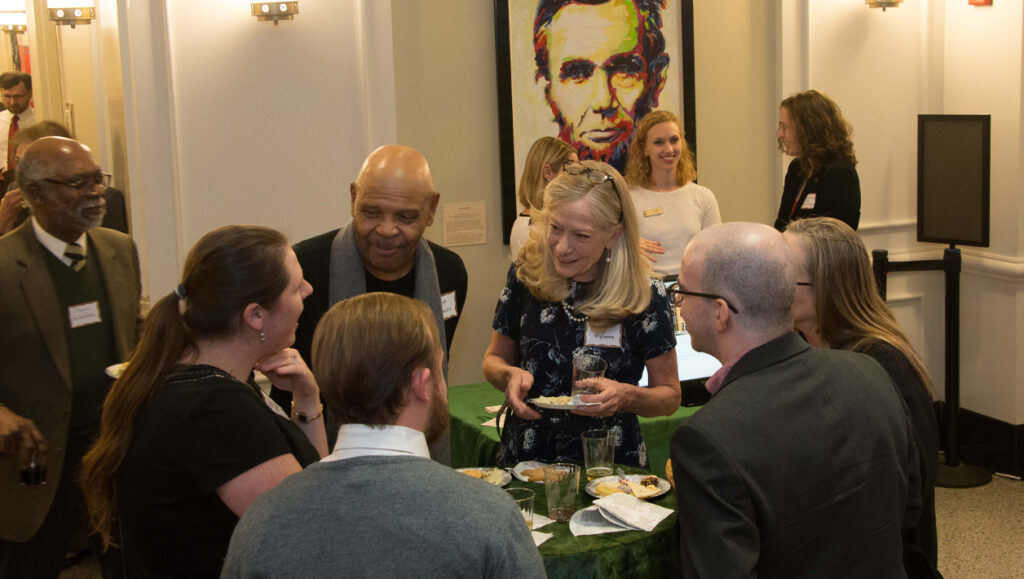 A group of people gather around a small table eating and talking.