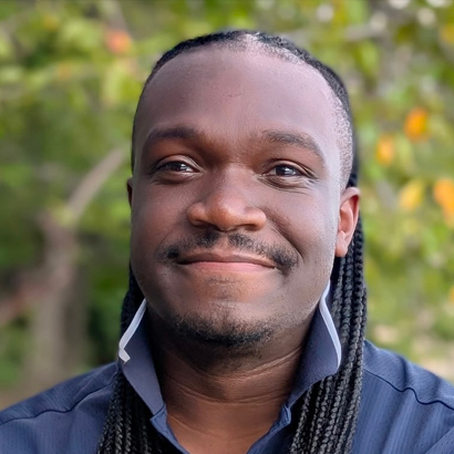 Headshot of a Black man with long dreadlocks wearing a blue shirt.