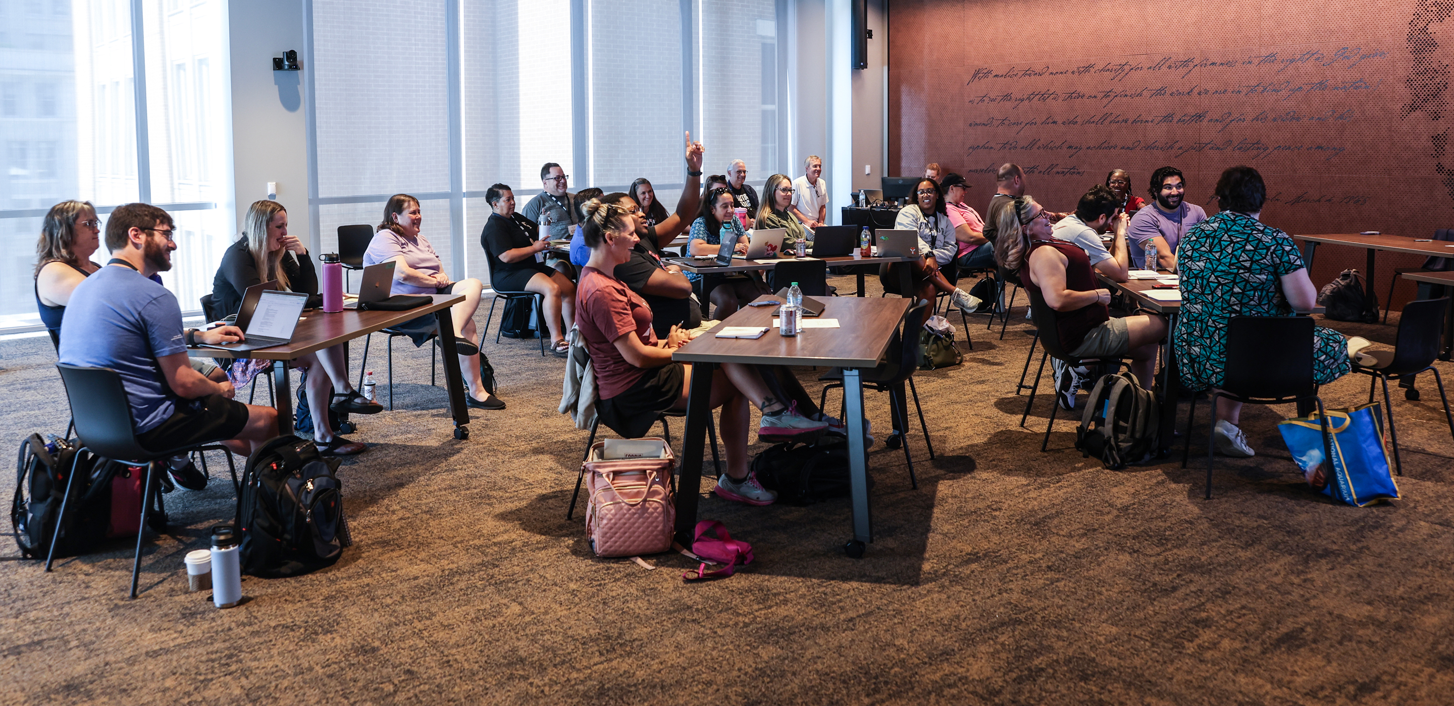 A group of 20 teachers in a meeting room and laughing and engaged in a presentation.