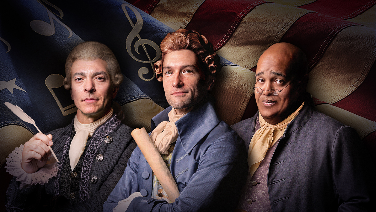 Two white men and a Black man dressed in colonial American clothing standing in front of a waving American flag.