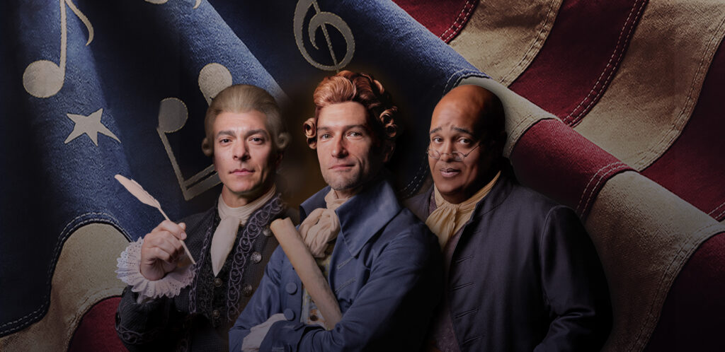 Two white men and a Black man dressed in colonial American clothing standing in front of a waving American flag.