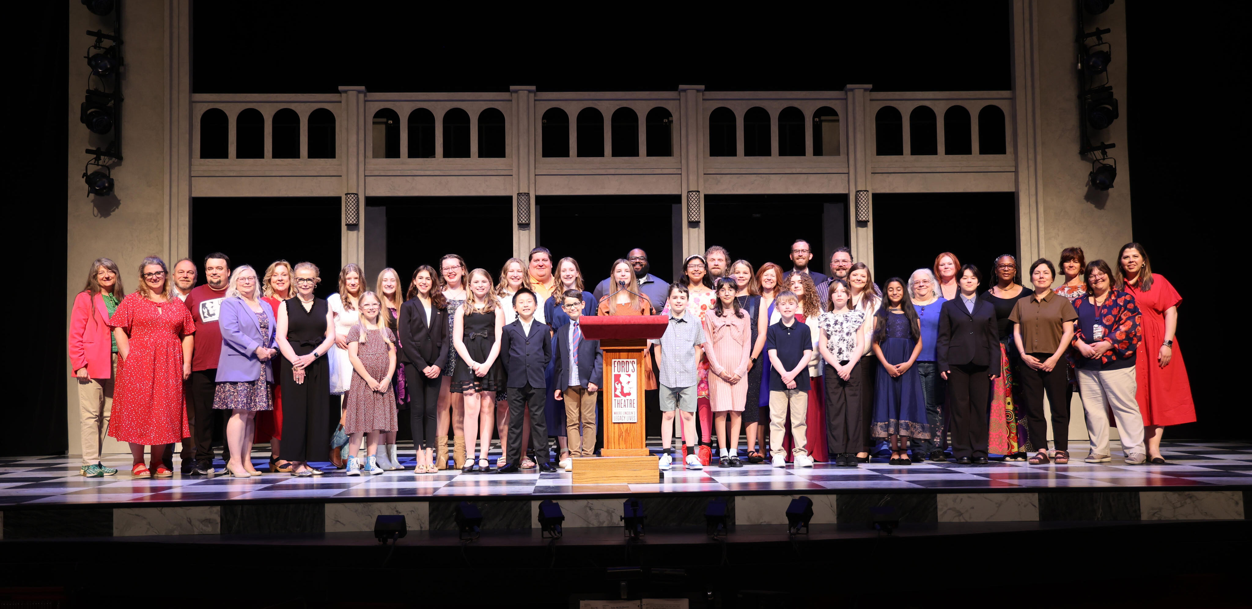 A group of children stand on a stage behind a Ford's Theatre podium.