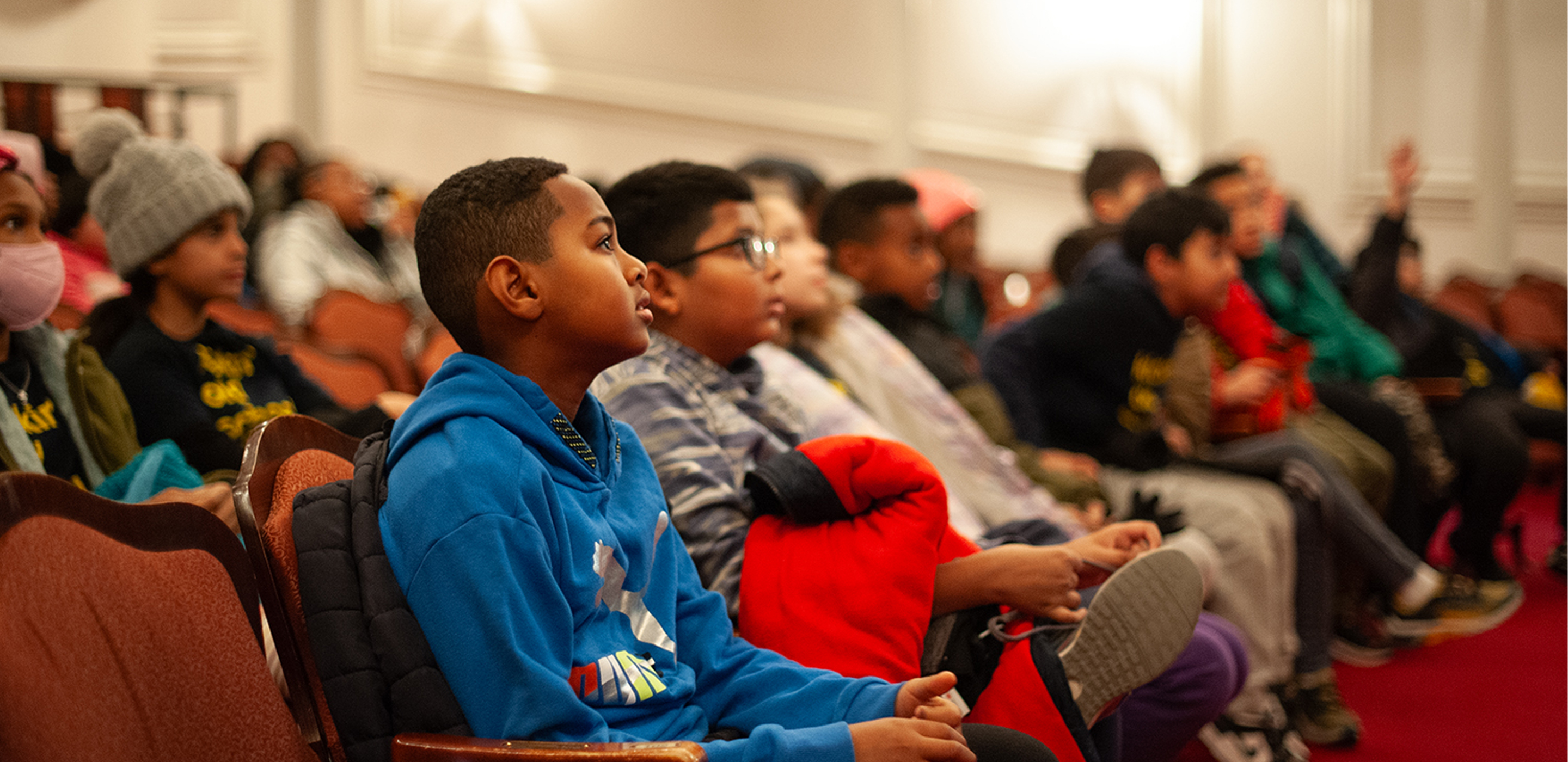 A group of young students sit in the audience of a theatre.