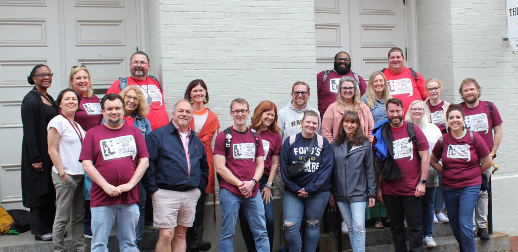 A group of a couple dozen people stand in front of Ford's Theatre and pose for the camera.
