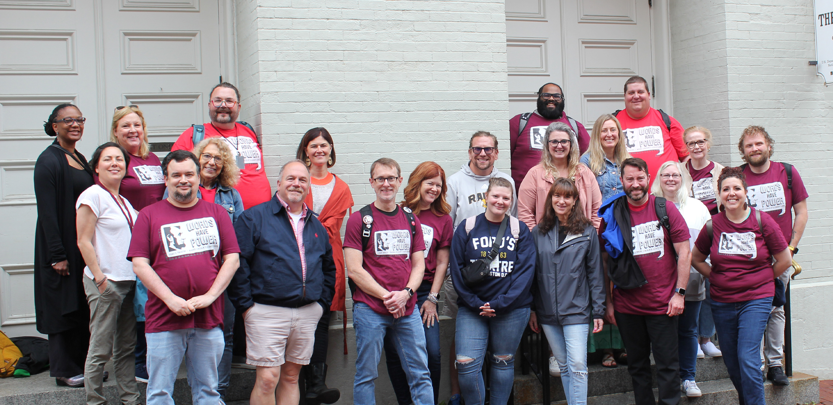 A group of a couple dozen people stand in front of Ford's Theatre and pose for the camera.