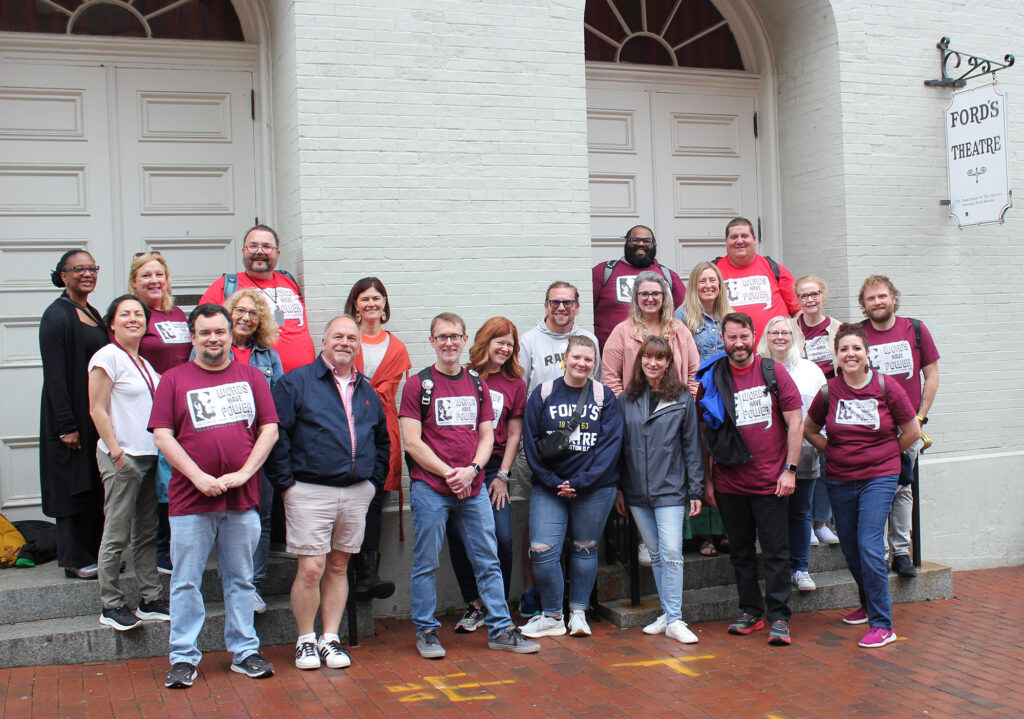 A group of a couple dozen people stand in front of Ford's Theatre and pose for the camera.