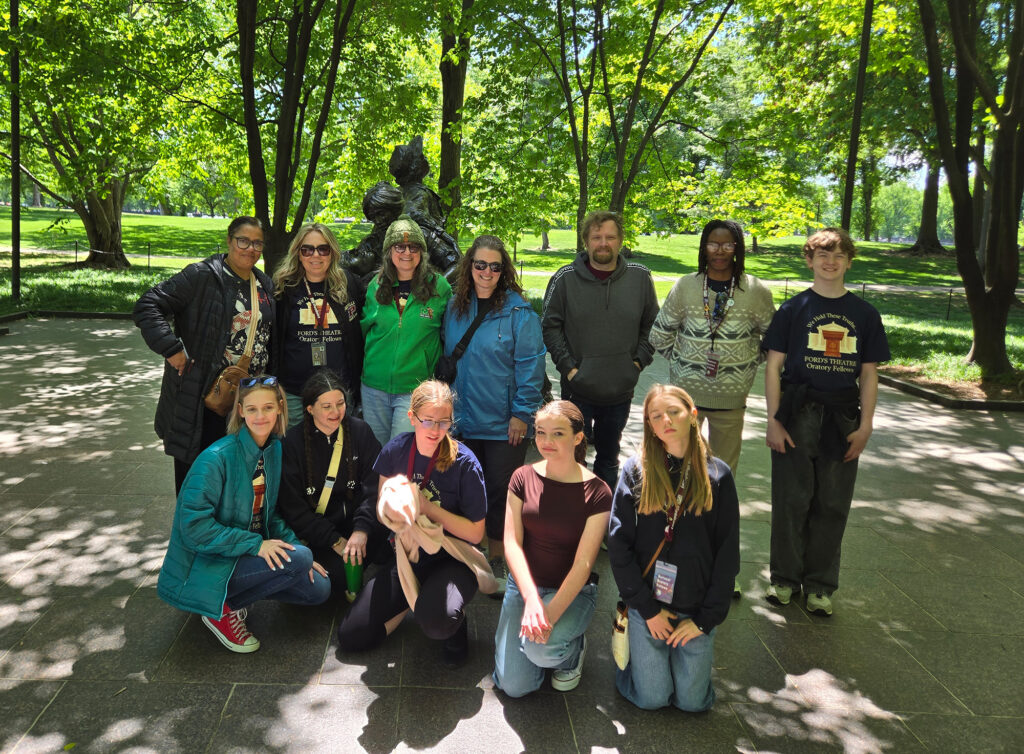 A group of adults and children stand in a park in front of a statue and pose for the camera.