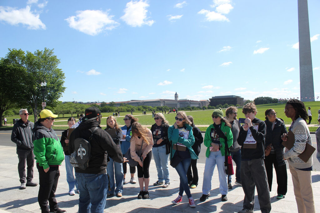 A group of people stand in a circle and talk, with the Washington Monument.